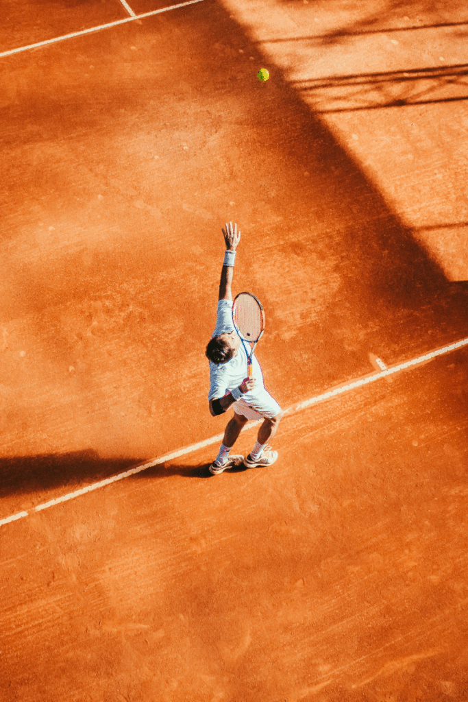 Aerial view of a tennis player executing a powerful serve on a clay court