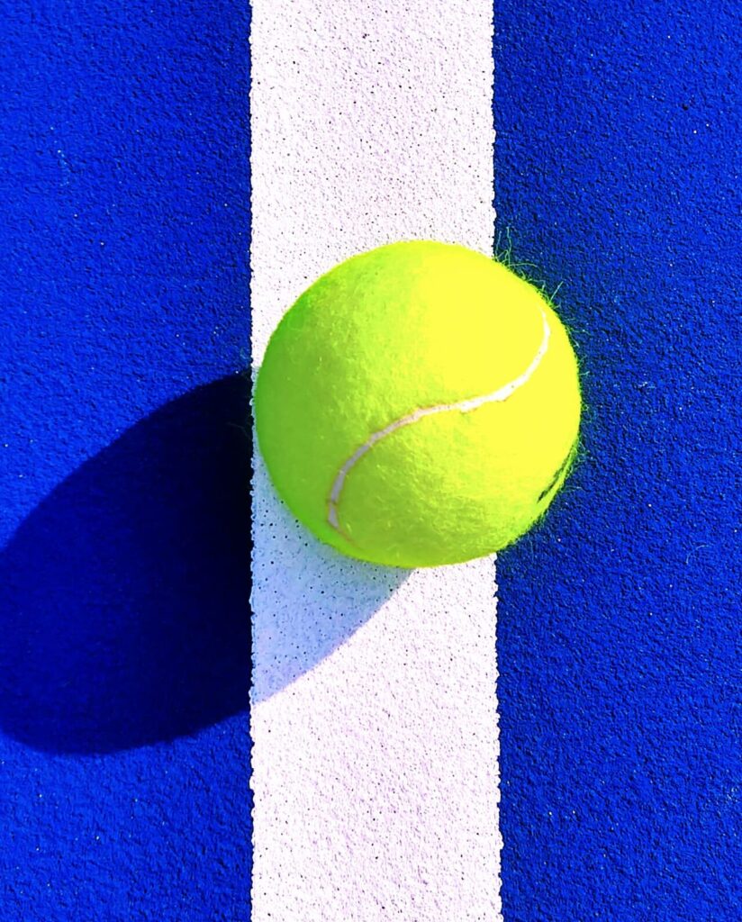 Tennis Ball on Court Line Closeup β Blue Hard Court Shadow Play Bright yellow tennis ball resting on the white line of a blue hard court with a long shadow.