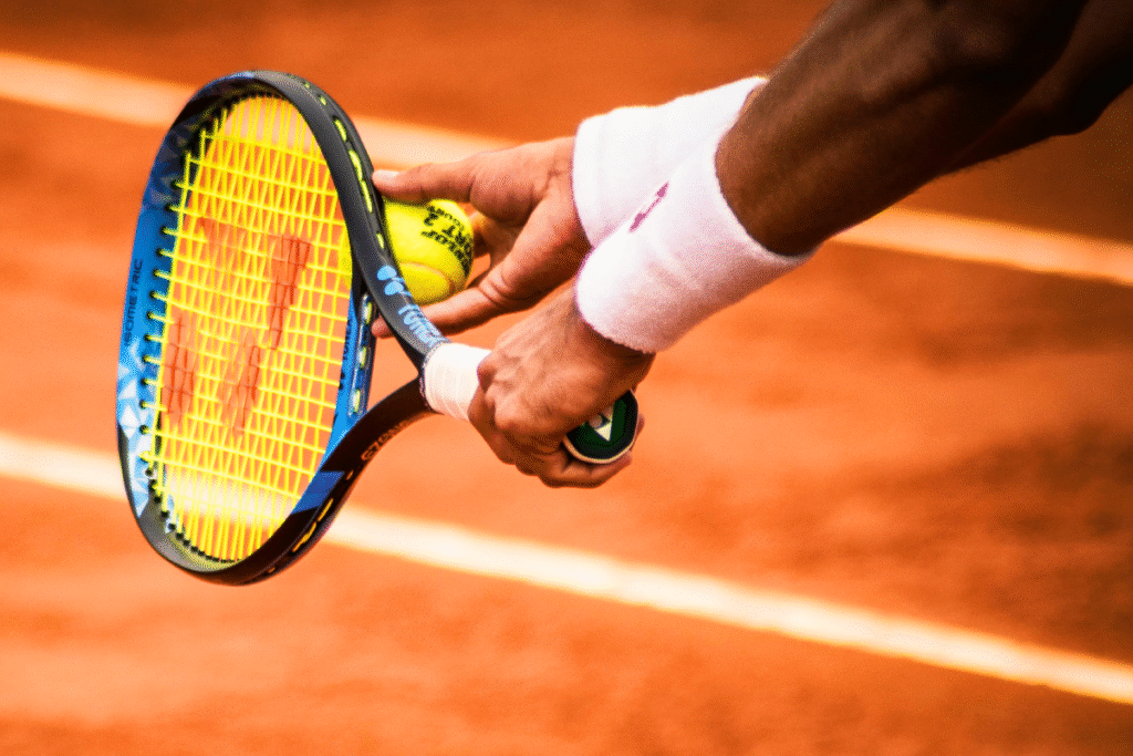 Tennis serve close-up showing player holding racket and ball on a clay court