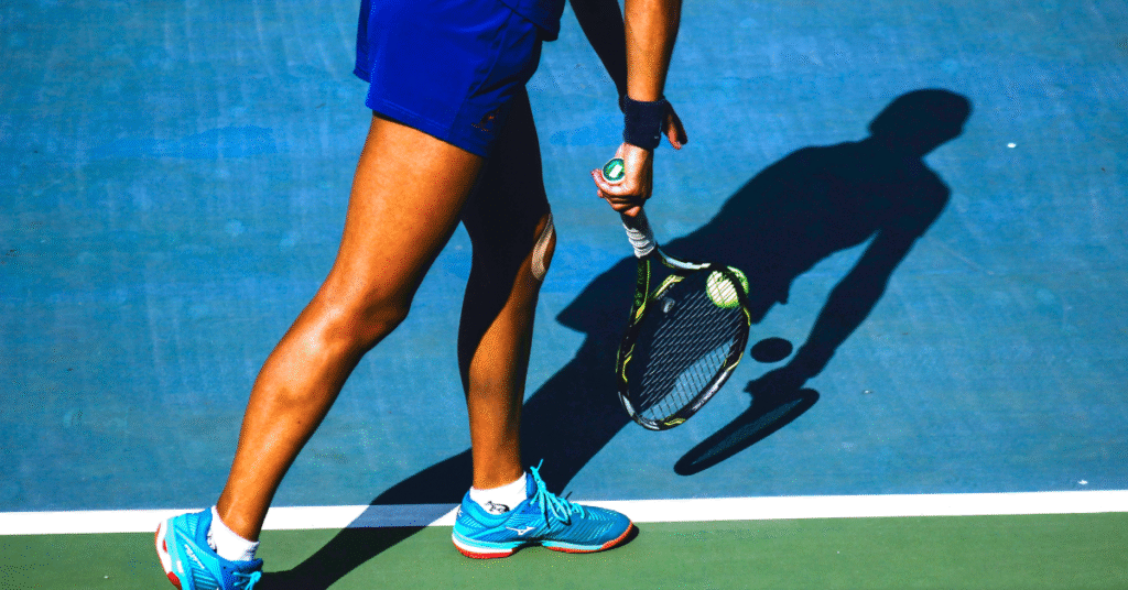 Tennis player preparing for a serve toss on a blue hard court, holding the ball and racket